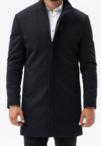 Svart, medellång kappa med en strukturerad design, med hög krage, zip-fickor och ett mjukt, texturerat tyg.