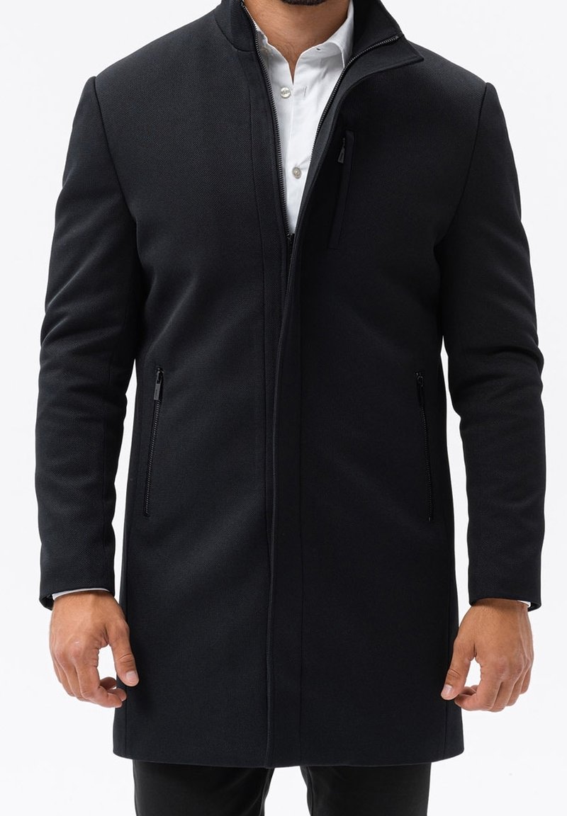 Svart, medellång kappa med en strukturerad design, med hög krage, zip-fickor och ett mjukt, texturerat tyg.