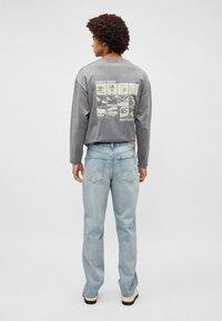 Γκρίζο πουκάμισο με μακριά μανίκια που διαθέτει γραφικό τύπωμα στην πλάτη με διάφορες εικόνες. Συνδυάζεται με ανοιχτό μπλε, φαρδιά τζιν παντελόνια.