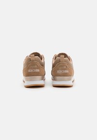 Chaussures de sport en daim marron avec une semelle extérieure blanche et beige, un col rembourré et une languette à l'arrière portant le logo "SKECHERS".