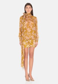 Completo con blusa floreale e gonna mini in giallo senape con fiori rosa; tessuto trasparente, maniche lunghe, collo alto e dettagli drappeggiati.