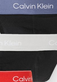 Calvin Klein Unterwäsche aus schwarzem Stoff mit elastischen Taillenbändern in Rot, Weiß und Blau, auf denen der Markenname in weißem Text angezeigt wird.