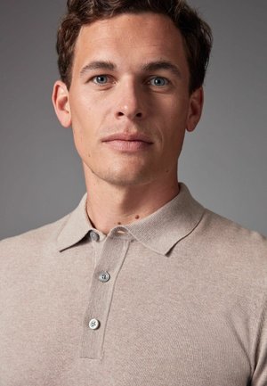 Polo beige con un punto texturizado, con un cuello clásico y tres botones grises. Tejido suave y detalles sutiles en toda la prenda.