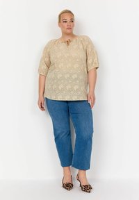 Top beige in pizzo con scollo a barca e dettaglio a chiave, abbinato a jeans blu a gamba dritta e tacchi alti con stampa leopardata.