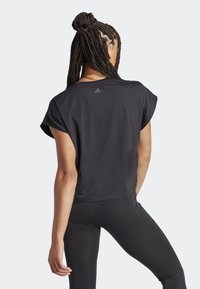 Camiseta deportiva negra de manga corta, con textura acanalada y un pequeño logo en la parte superior de la espalda. Combinada con leggins negros de diseño ajustado.
