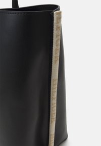 Zwarte leren tas met een gestructureerde vorm, voorzien van een textuur accent in beige stof langs een rand. Minimalistisch ontwerp zonder zichtbare hardware.