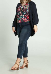 Top con estampado floral en colores vivos, cárdigan azul marino, jeans oscuros y sandalias de tacón marrones con tiras.