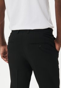 Pantalones negros de vestir con una textura suave, que cuentan con dos bolsillos traseros y botones, combinados con una camisa blanca sencilla.