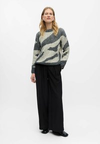 Maglione a maglia con motivo astratto grigio e crema, texture a coste, colletto rotondo; abbinato a pantaloni larghi neri e scarpe nere.