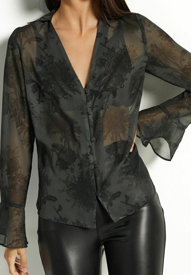Transparente schwarze Bluse mit floralem Muster, tiefem V-Ausschnitt, langen Glockenärmeln und Knopfleiste, mit dezenten Mustern und leichtem, fließendem Stoff.