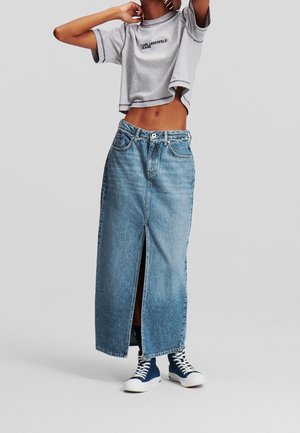 T-shirt gris court avec logo, associé à une jupe longue en denim taille haute et ample, avec une fente devant et des accents bleus, portée avec des baskets.