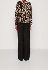 Haut à manches longues imprimé léopard avec un design à trou de serrure dans le dos, associé à un pantalon noir ample, tous deux avec des textures douces.