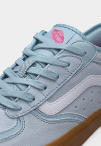 Ανοιχτό μπλε αθλητικό παπούτσι Vans με λευκή πλευρική ρίγα, μπλε κορδόνια στο ίδιο χρώμα, ροζ λογότυπο Vans "Off The Wall" στη γλώσσα και σόλα από καουτσούκ σε χρώμα τσίχλας.