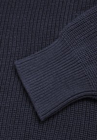 Marineblauwe gebreide trui stof met een gestructureerd, ribbelpatroon. Heeft een gevouwen manchet detail. Het materiaal lijkt zacht en dicht te zijn.