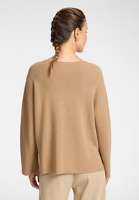 Maglione a coste beige con scollo ampio, spalle abbassate e vestibilità rilassata, abbinato a pantaloni beige; dettaglio del tessuto testurizzato visibile.