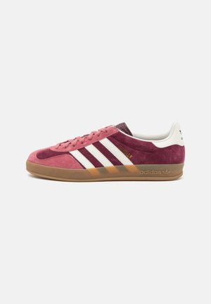 Sneaker Adidas in suede rosa con strisce bianche e suola in gomma marrone. Presentano dettagli testurizzati e un design a profilo basso.