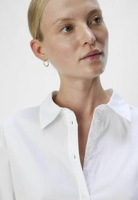 Biała koszula z guzikami z klasycznym kołnierzykiem, charakteryzująca się prostymi liniami, lekkim materiałem i małymi detalami guzików w okolicy dekoltu.