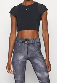 Černý krátký sportovní top s krátkými rukávy a reflexním logem, kombinovaný s vysokým pasem, šedými legínami s texturou a abstraktním vzorem.