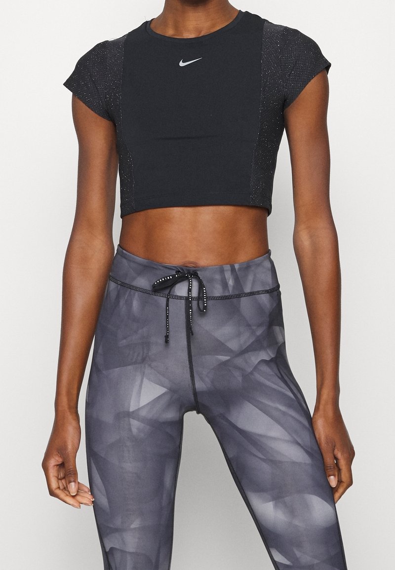 Musta, lyhyillä hihoilla varustettu lyhennetty urheilutoppi, jossa on heijastava logo, yhdistetty korkeavyötäröisiin, teksturoituihin harmaisiin leggingsseihin, joissa on abstrakti kuvio.