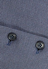 Knapp-up skjorttyg i marinblått med ett strukturerat mönster. Har två svarta plastknappar, var och en med fyra hål, med kontrasterande sömnad.