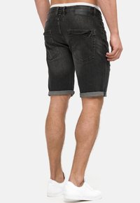 Zwarte denim shorts met opgerolde omslagen, voorzien van twee achterzakken en een leren label op de tailleband. Draagt met witte sneakers.