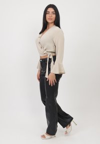 Haut beige à manches évasées avec des boutons en bois, associé à un pantalon noir en simili cuir et des talons blancs à fines lanières.