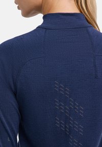 Granatowa sportowa koszulka z długim rękawem, z wysokim kołnierzem, teksturowanej tkaniny oraz subtelnym refleksyjnym wzorem na plecach zwiększającym widoczność.