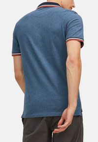 Męska koszulka polo w niebieskim kolorze, z czarnym i czerwonym paskiem na kołnierzu oraz mankietach, o gładkiej fakturze i dopasowanym kroju.