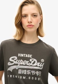 Mørkegrå bomulds T-shirt med et glitrende, holografisk "SuperDry"-logo og tekst, med rund hals og korte ærmer.