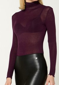 Langärmliger, figurbetonter Rollkragenpullover aus transparentem dunkelviolettem Stoff; verfügt über eine glatte Textur und leicht geraffte Bündchen. Kombiniert mit schwarzen Leggings.