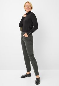 Maglione a collo alto nero a maniche lunghe, pantaloni slim-fit verde oliva e mocassini neri, caratterizzati da dettagli minimi e una superficie liscia.