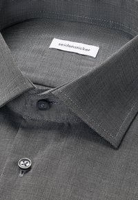 Nahaufnahme eines hellgrau gemusterten Hemdkragens mit schwarzen Knöpfen und einem weißen Etikett mit der Aufschrift "seidensticker."