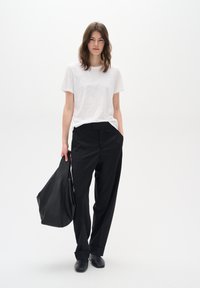 Tricou alb cu guler rotund, purtat împreună cu pantaloni negri cu talie înaltă. Modelul ține o geantă mare, texturată, de culoare neagră și poartă pantofi slip-on negri.