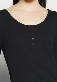 Svart långärmad topp med ribbat struktur, vid rundad halsringning och femknapps knappslå fram.