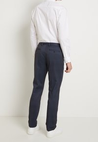 Pantalones de cuadros azul marino con corte ajustado, confeccionados en tejido ligero. Cuentan con dos bolsillos traseros y una cintura lisa. Combinados con una camisa blanca de vestir.