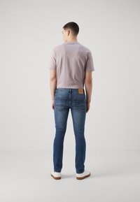 Camiseta de manga corta de color púrpura claro combinada con jeans ajustados de color azul oscuro que presentan un parche de cuero marrón en la cintura y zapatillas blancas.