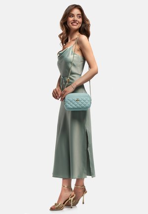 Abito in satin verde chiaro con spacco laterale, abbinato a una borsa trapuntata blu chiaro e a tacchi a strappo metallici oro. La modella ha i capelli lunghi.