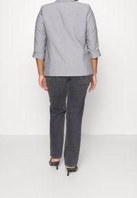 Grau maßgeschneiderte Blazer mit Dreiviertelärmeln, kombiniert mit dunklen Jeans und schwarzen High-Heels. Glatter Stoff und strukturiertes Design.
