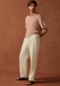 Struktureret, rustfarvet polo med kortærmer og v-hals, parret med lyse beige, afslappede bukser og brune sandaler.