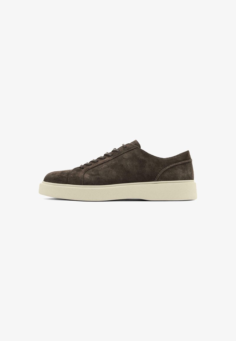 Sneaker in suede marrone con una texture liscia, punta rotonda, suola piatta in gomma e un design semplice con lacci. Cuciture sottili sui lati.