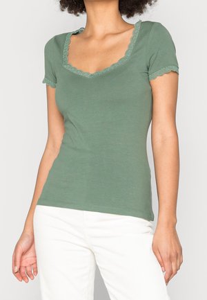 Top verde a maniche corte con scollatura e orlo a zigzag. Realizzato in un tessuto morbido, design aderente con delicati accenti in pizzo sulle maniche e sulla scollatura.