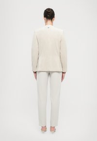 Blazer in corduroy beige chiaro con un design strutturato, abbinato a pantaloni grigi chiari su misura. Presenta una superficie liscia e una schiena aperta.