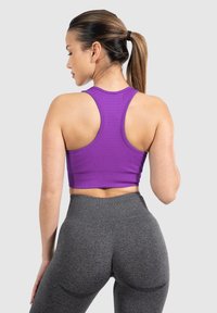 Top deportivo corto en color morado con diseño acanalado y espalda de nadador, combinado con leggings de cintura alta en gris oscuro. Textura suave y silueta entallada.