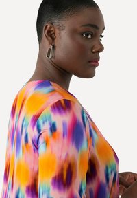 Blusa multicolor con estampado en tonos naranja, morado y azul, de textura suave, con cuello redondo y mangas largas.