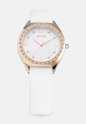 Montre avec bracelet en silicone blanc, boîtier argenté et lunette en or rose ornée de cristaux, avec un cadran blanc texturé et aiguilles dorées.
