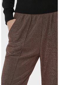 Csillogó barna nadrág laza szabással, elasztikus derékpánttal és puha, texturált anyagból, a fokozott kényelem érdekében.