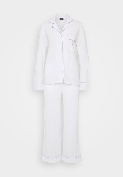 Λευκή πιτζάμα, ελαφρύ ύφασμα, με μπλε ρέλι γύρω από τον γιακά, την τσέπη και τα τελειώματα των παντελονιών. Μακριά μανίκια και χαλαρά παντελόνια.