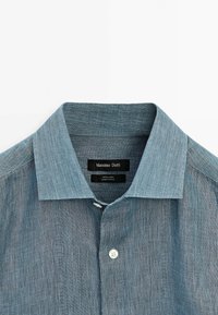 Chemise en lin bleu à col de Massimo Dutti avec boutons apparents et texture, étiquetée 100 % lin et fabriquée en Chine.