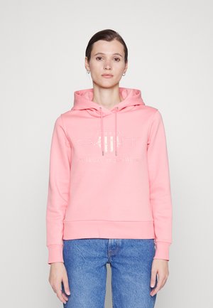 Pink cotton hoodie with a front logo, adjustable drawstrings, and ribbed cuffs. Paired with blue jeans for a casual look.