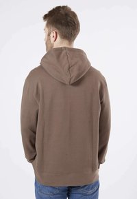 Sweatshirt à capuche marron avec une coupe décontractée, texture douce et poignets côtelés, associé à un jean bleu. Vue de derrière.